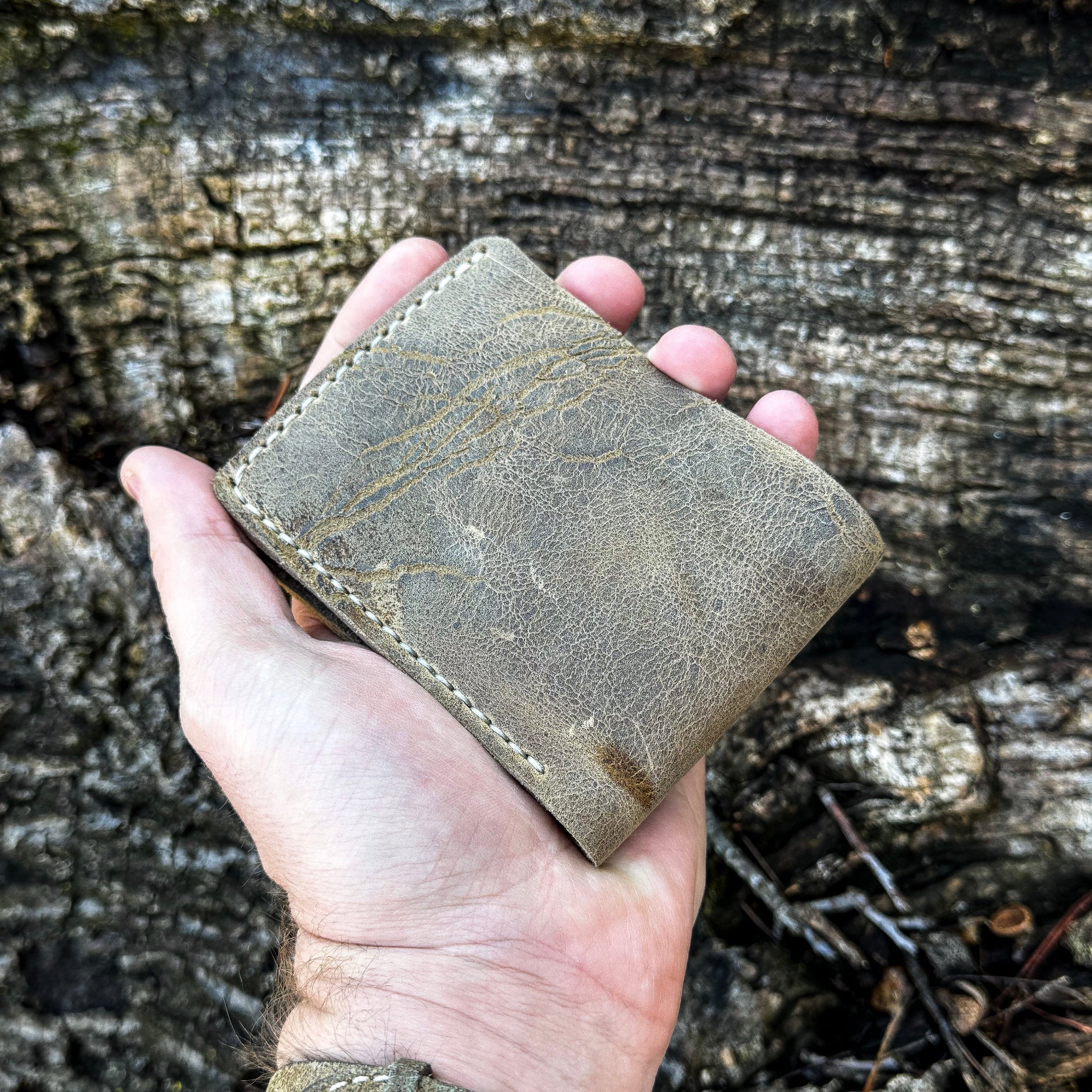 Hand holding the closed handcrafted No. 1652 JAGTER field bifold wallet in Desert color Wild African Kudu leather, showing its compact pocket size and natural exterior texture.