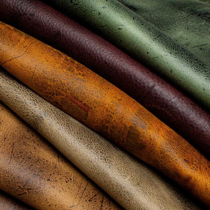 A vibrant, close-up collection shot of various C.F. Stead & Co Kudu leather hides, showcasing the diverse color palette, unique natural scarring, and rugged, character-filled grain patterns characteristic of this premium exotic leather.
