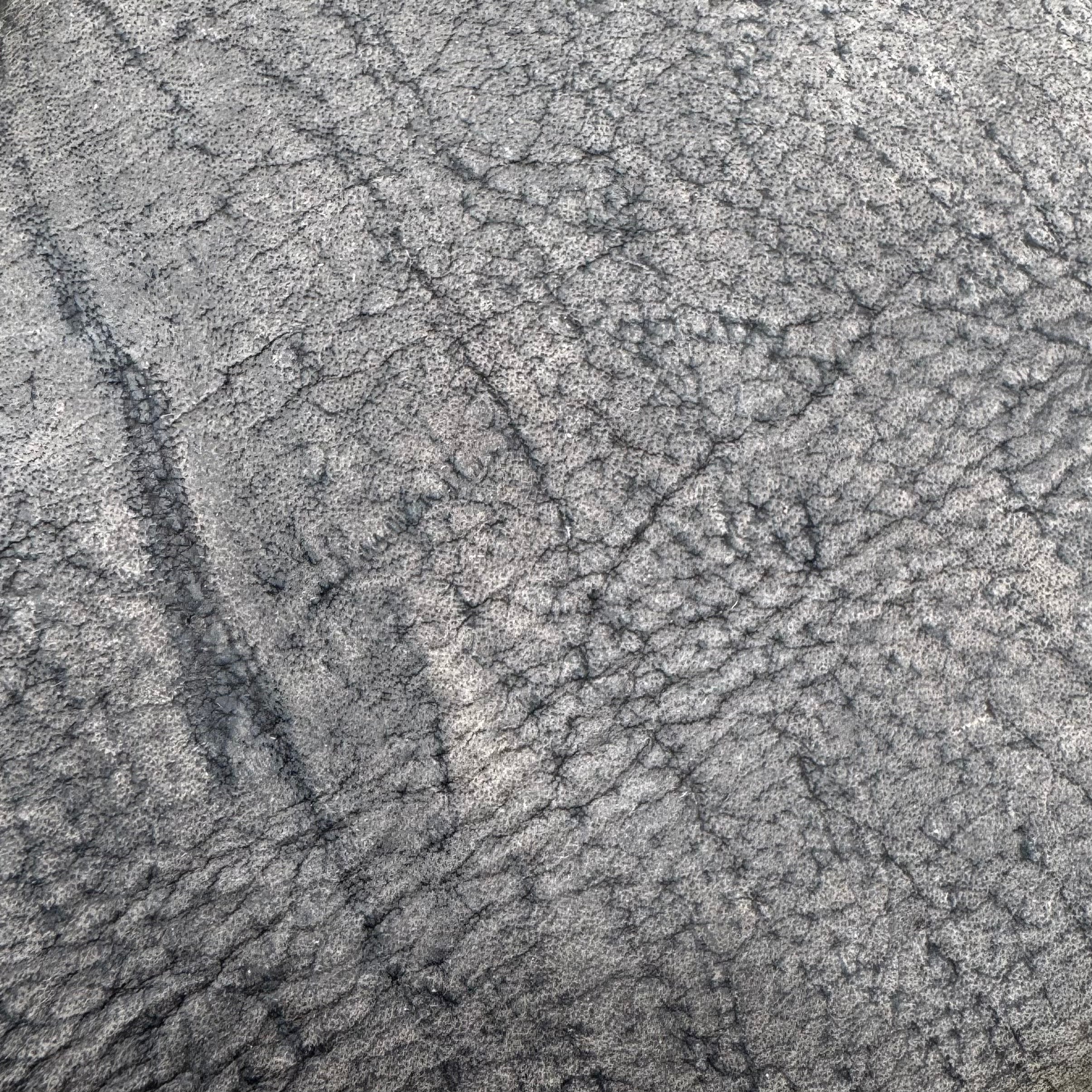 An extreme macro close-up of a raw Charred Earth Wild African Kudu leather hide, showcasing its rugged natural grain, deep organic striations, and unique wild habitat scars in ashy grey and charcoal tones.