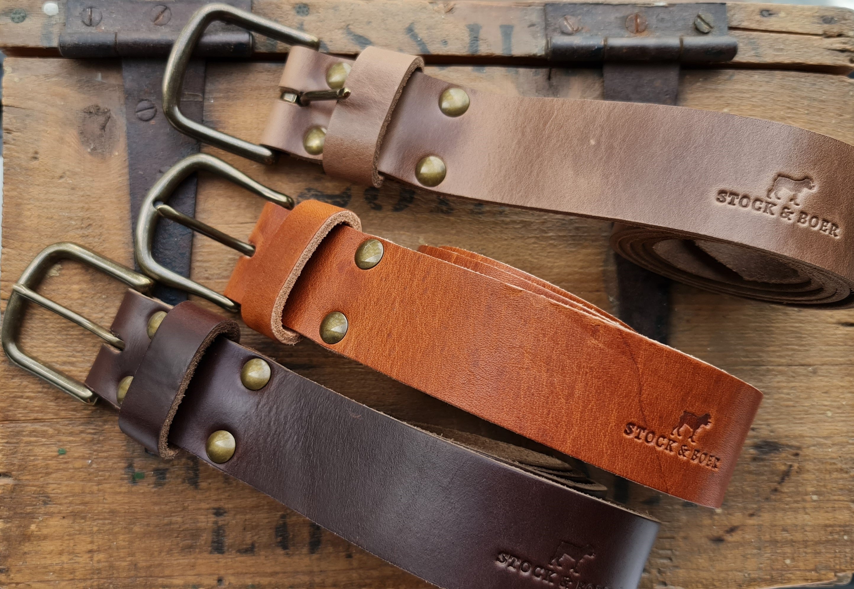 An overview of three Horween belts—natural Chromexcel, English Tan Dublin, and burgundy Chromexcel—each stamped with the Stock & Boer logo.