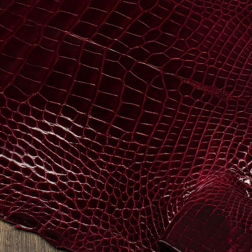 Macro texture shot of a rich Bull's Blood burgundy HCP Tannery alligator hide, focusing on the intricate, geometric pattern and natural depth of the premium exotic scales.