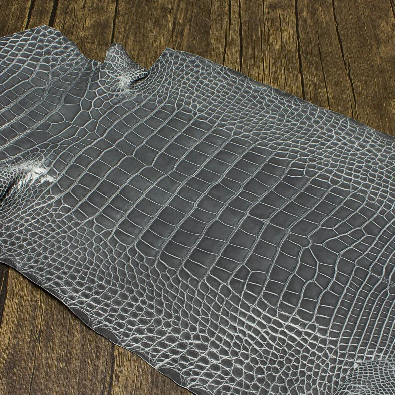An overhead perspective of a premium Ghost grey HCP Tannery alligator hide, displaying the natural, symmetrical scale structure and elegant finish of the exotic skin laid against a rustic wooden surface.