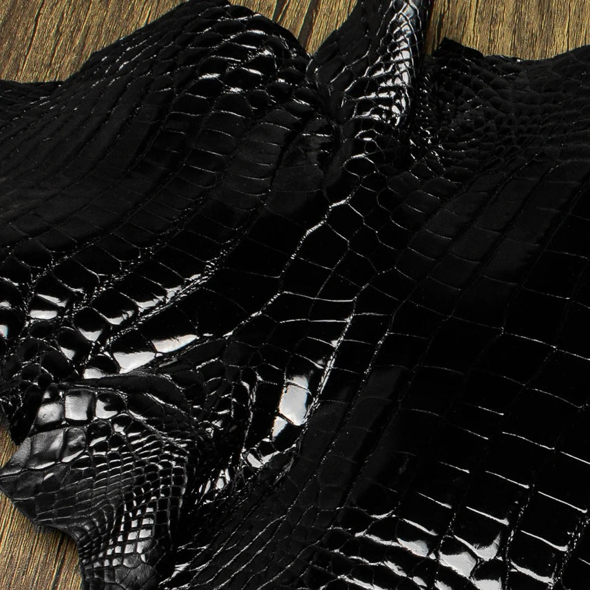 An overhead perspective of a premium Midnight Black HCP Tannery alligator hide, displaying the natural, symmetrical scale structure and elegant finish of the exotic skin laid against a rustic wooden surface.