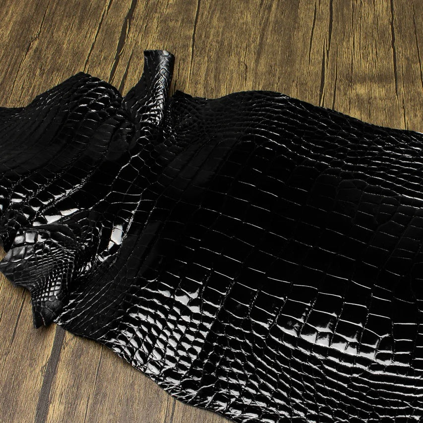 An overhead perspective of a premium Midnight Black HCP Tannery alligator hide, displaying the natural, symmetrical scale structure and elegant finish of the exotic skin laid against a rustic wooden surface.