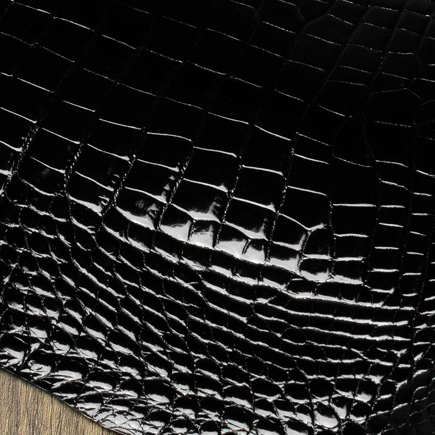 Macro texture shot of a premium Midnight Black HCP Tannery alligator hide, focusing on the intricate, geometric pattern and natural depth of the exotic scales.