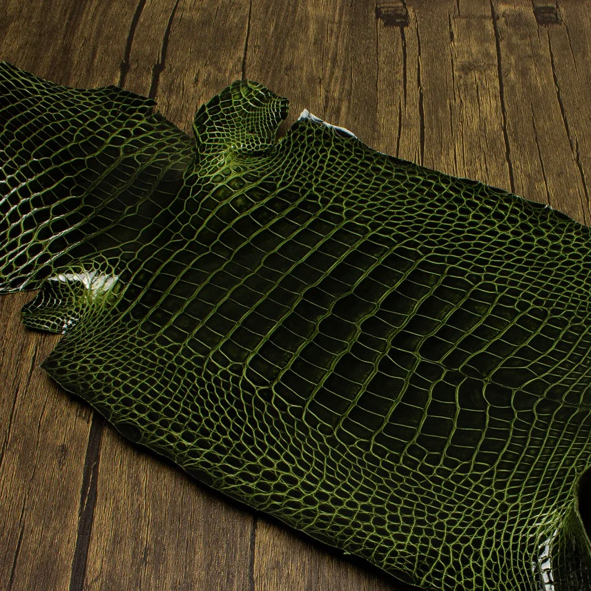 An overhead perspective of a premium River green HCP Tannery alligator hide, displaying the natural, symmetrical scale structure and elegant finish of the exotic skin laid against a rustic wooden surface.