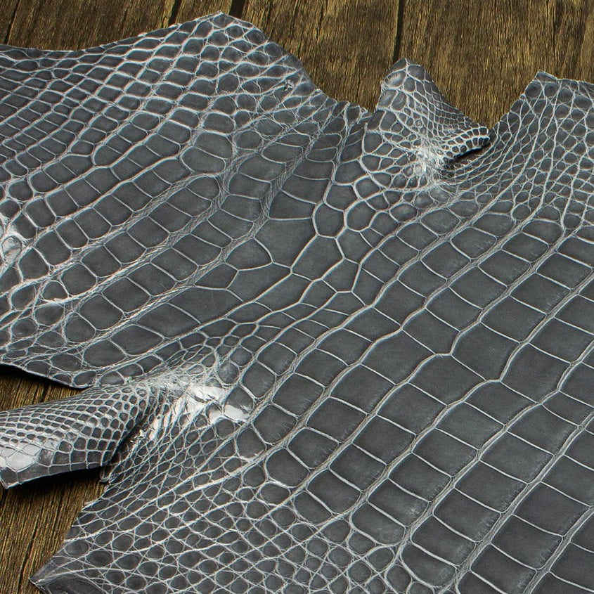 An overhead perspective of a premium Ghost grey HCP Tannery alligator hide, displaying the natural, symmetrical scale structure and elegant finish of the exotic skin laid against a rustic wooden surface.