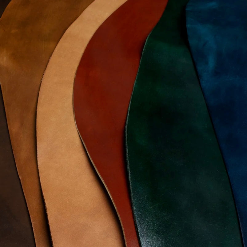 A vibrant, layered display showcasing a colorful assortment of premium Horween Shell Cordovan leather hides, including tan, red, green, and blue.