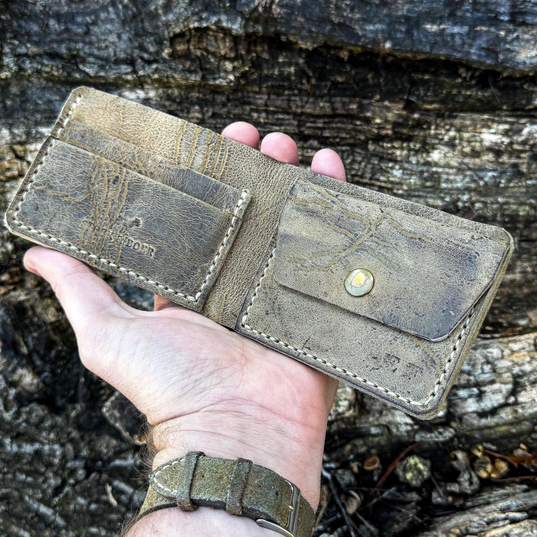 Hand holding the open interior of the handcrafted No. 1652 JAGTER field bifold wallet in Desert color Wild African Kudu leather, showcasing card slots and a snap-closure coin pouch.