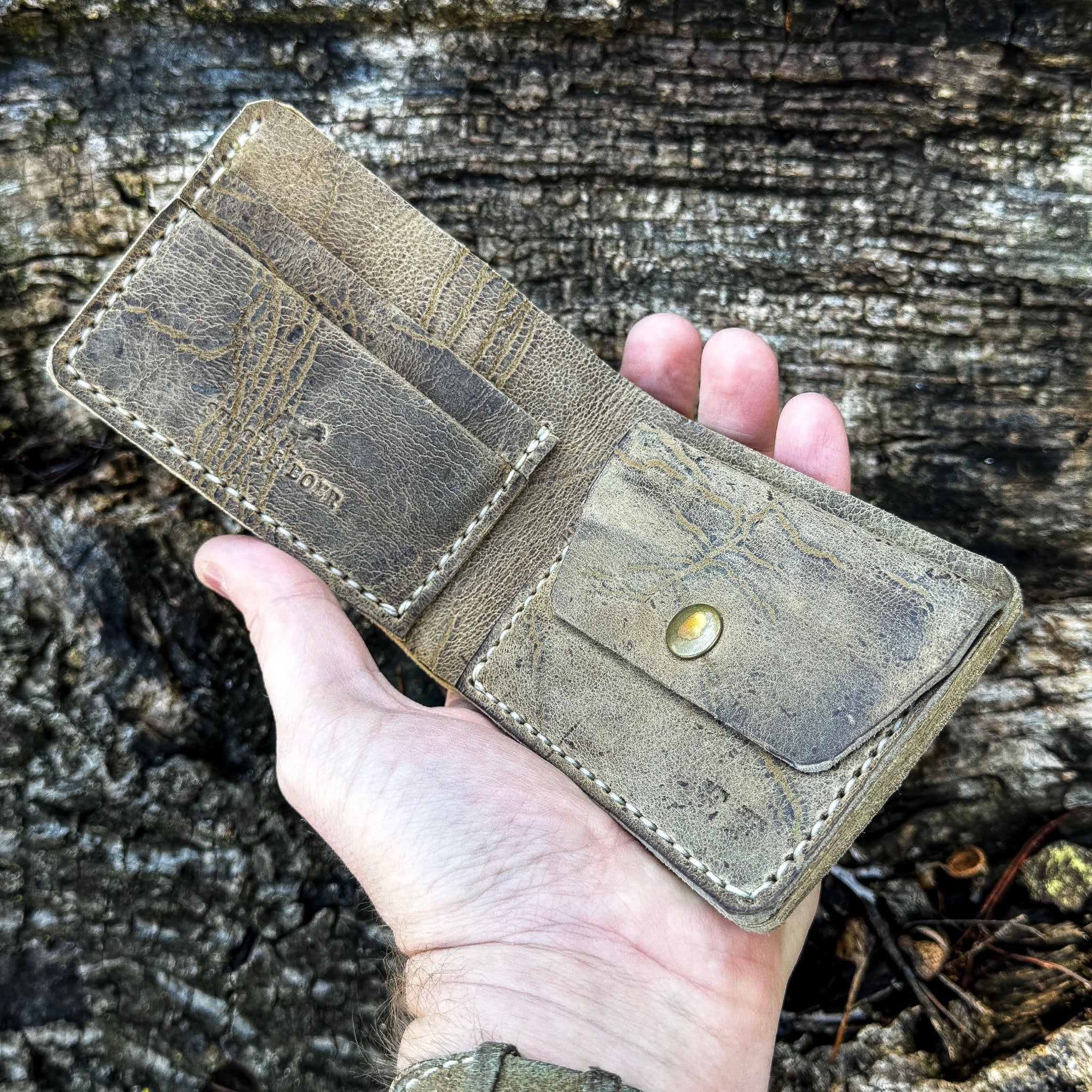 A hand holding the open handcrafted No. 1652 JAGTER field bifold wallet in Desert color Wild African Kudu leather, showcasing the complete interior layout including multiple card slots and a utility snap coin pouch.
