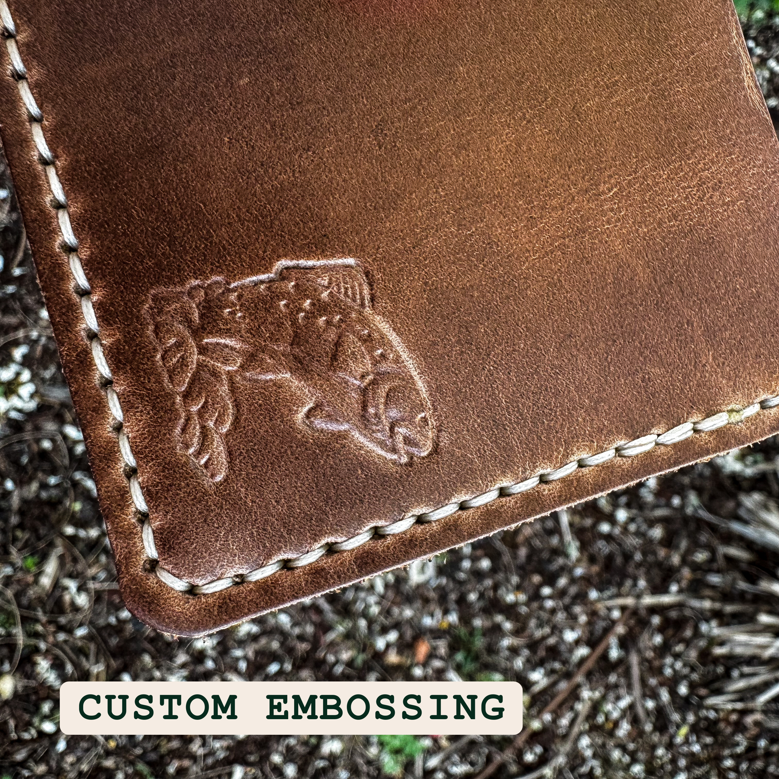 A close-up view of custom trout embossing on the No. 2 FRONTIERSMAN Leather Bifold Wallet. The image highlights the detailed debossed fish design, the rich texture of the leather, and the precise hand-stitching along the edge.