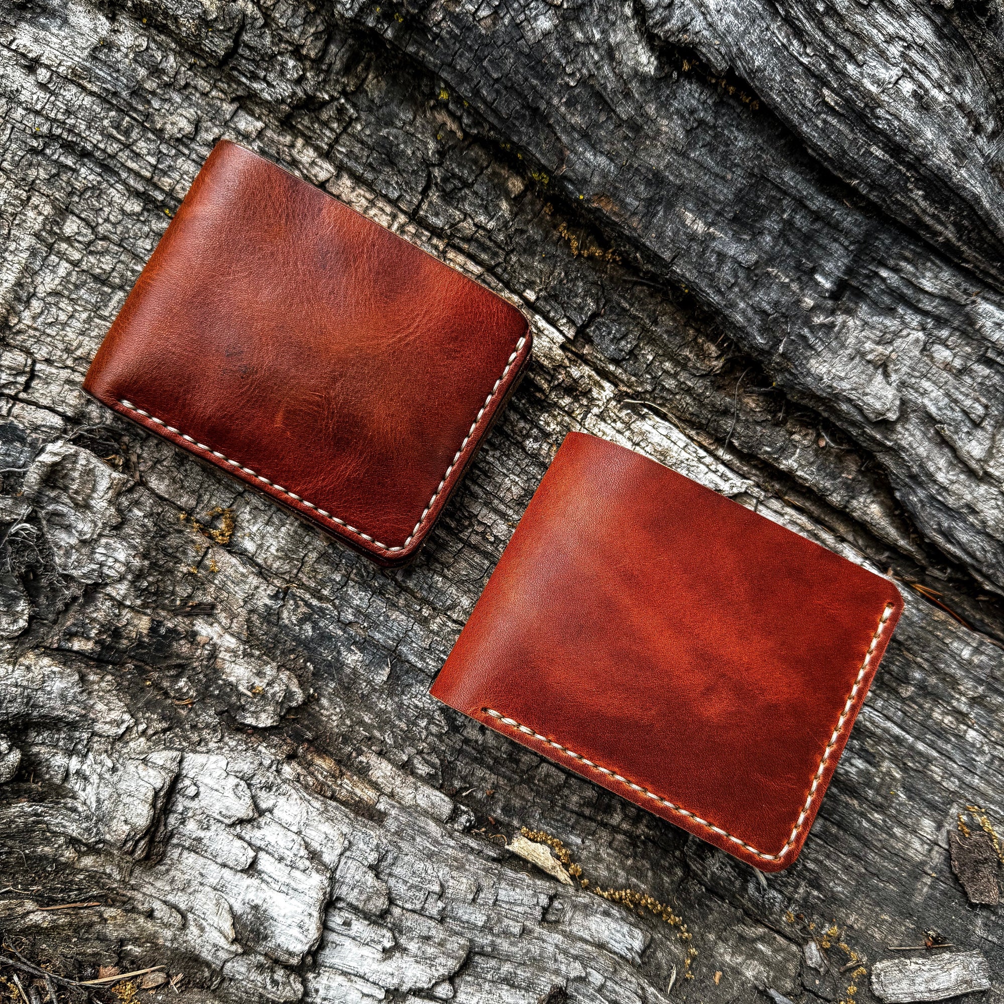 A pair of No. 2 FRONTIERSMAN Leather Bifold Wallets, both crafted from Horween English Tan Dublin leather, displayed side-by-side on a textured, rugged bark background. The image showcases the consistent finish, minimalist bifold design, and detailed contrast stitching of both pieces.