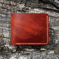 The No. 2 FRONTIERSMAN Leather Bifold Wallet, crafted from Horween English Tan Dublin leather, resting on a textured bark surface. The image showcases the wallet's clean, minimalist bifold design and precise contrast stitching.