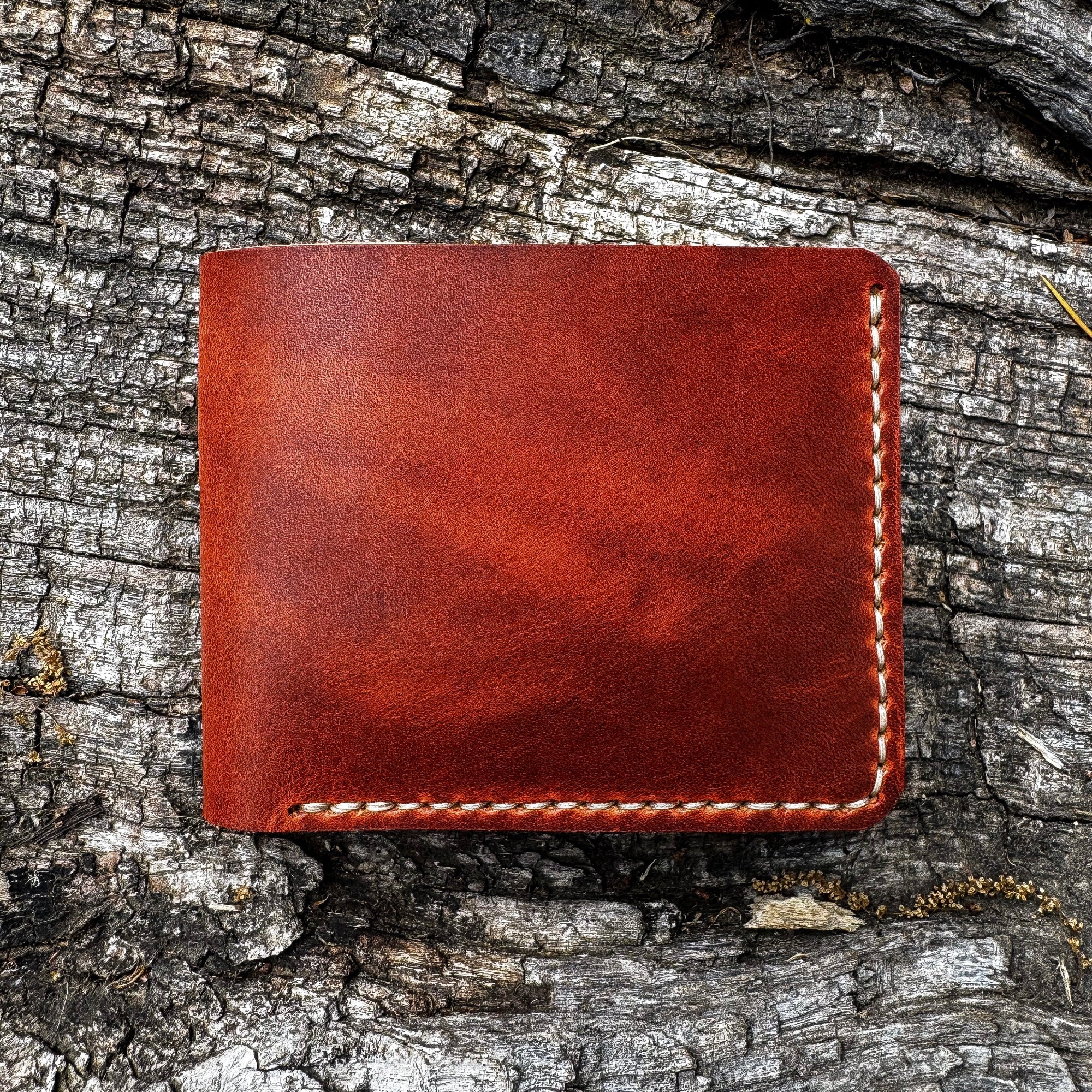 The No. 2 FRONTIERSMAN Leather Bifold Wallet, crafted from Horween English Tan Dublin leather, resting on a textured bark surface. The image showcases the wallet's clean, minimalist bifold design and precise contrast stitching.