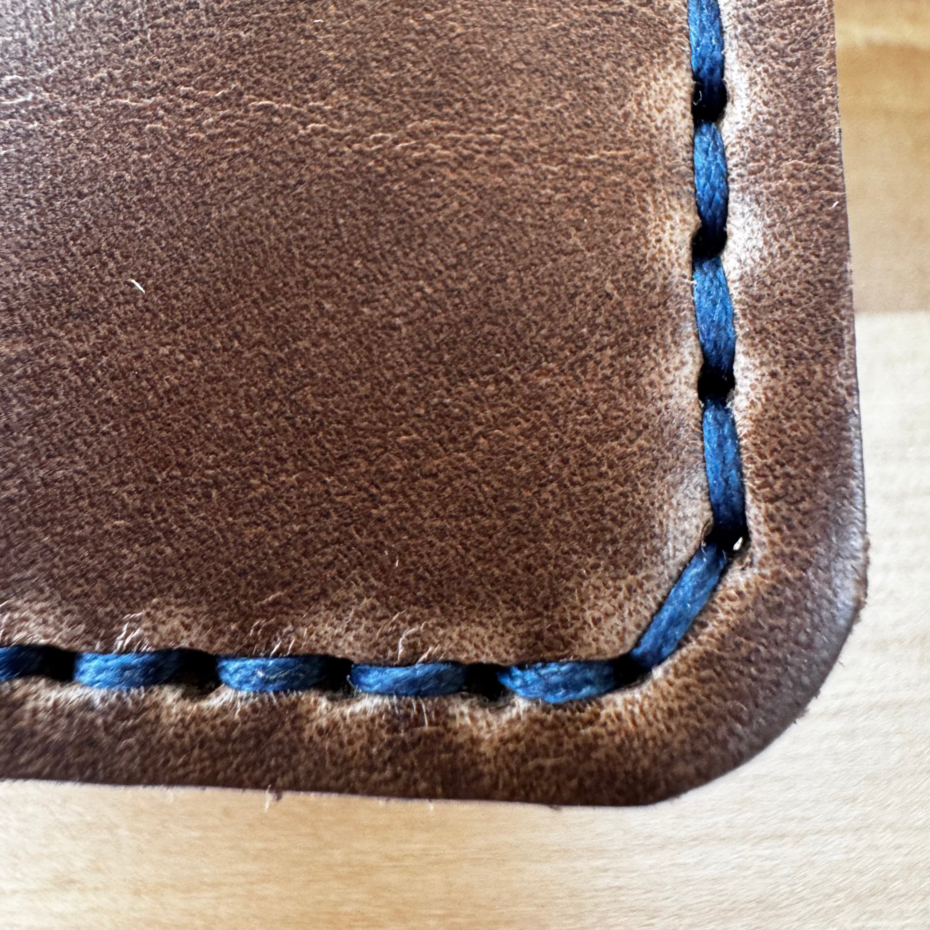 A detailed close-up view of the No. 2 FRONTIERSMAN Leather Bifold Wallet, crafted from natural Horween Chromexcel leather with striking navy blue stitching. The image focuses on the quality of the hand-stitched corner, highlighting the contrast between the rich brown leather and the vibrant navy thread.
