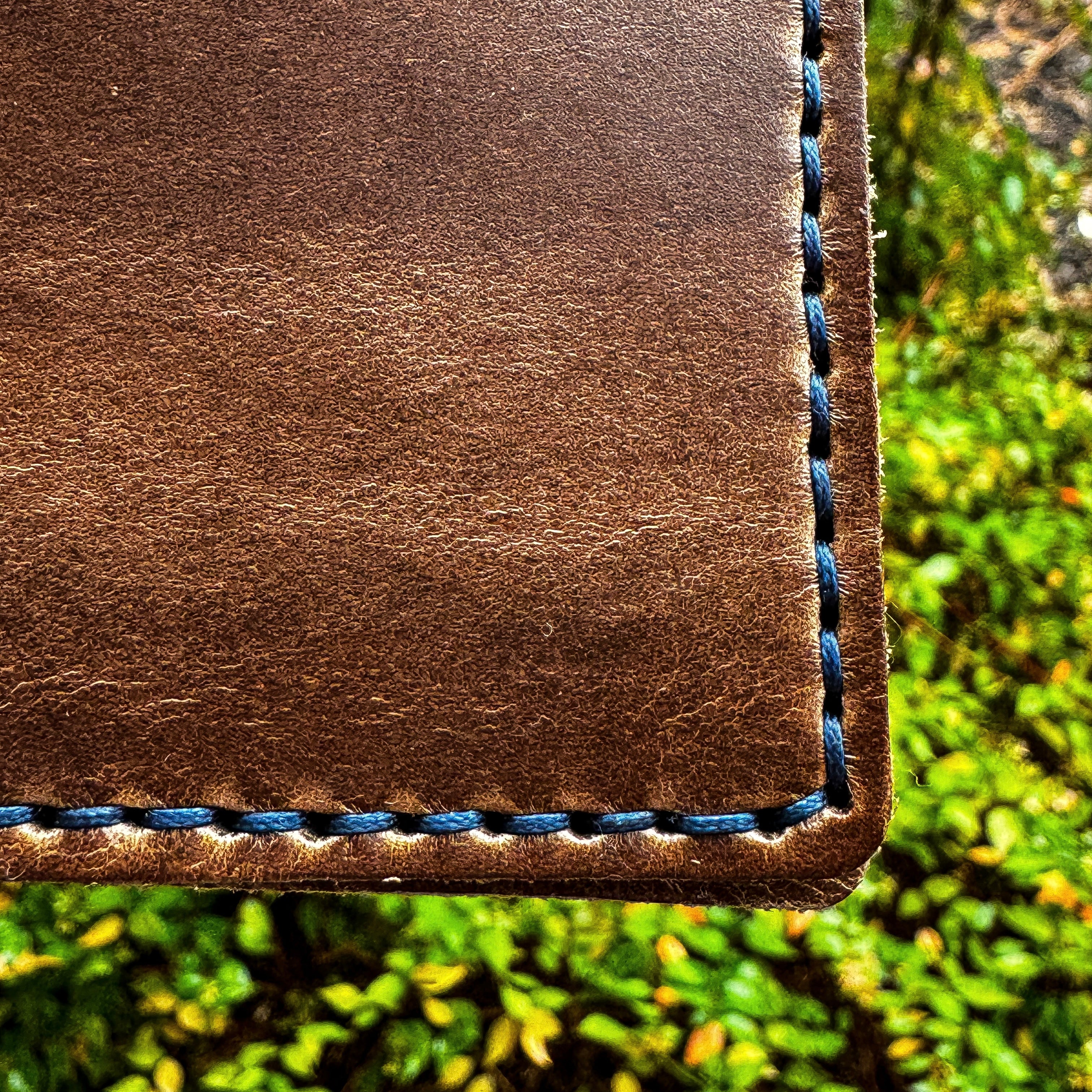 A detailed close-up view of the No. 2 FRONTIERSMAN Leather Bifold Wallet, crafted from natural Horween Chromexcel leather with striking navy blue stitching. The image focuses on the quality of the hand-stitched corner, highlighting the contrast between the rich brown leather and the vibrant navy thread.