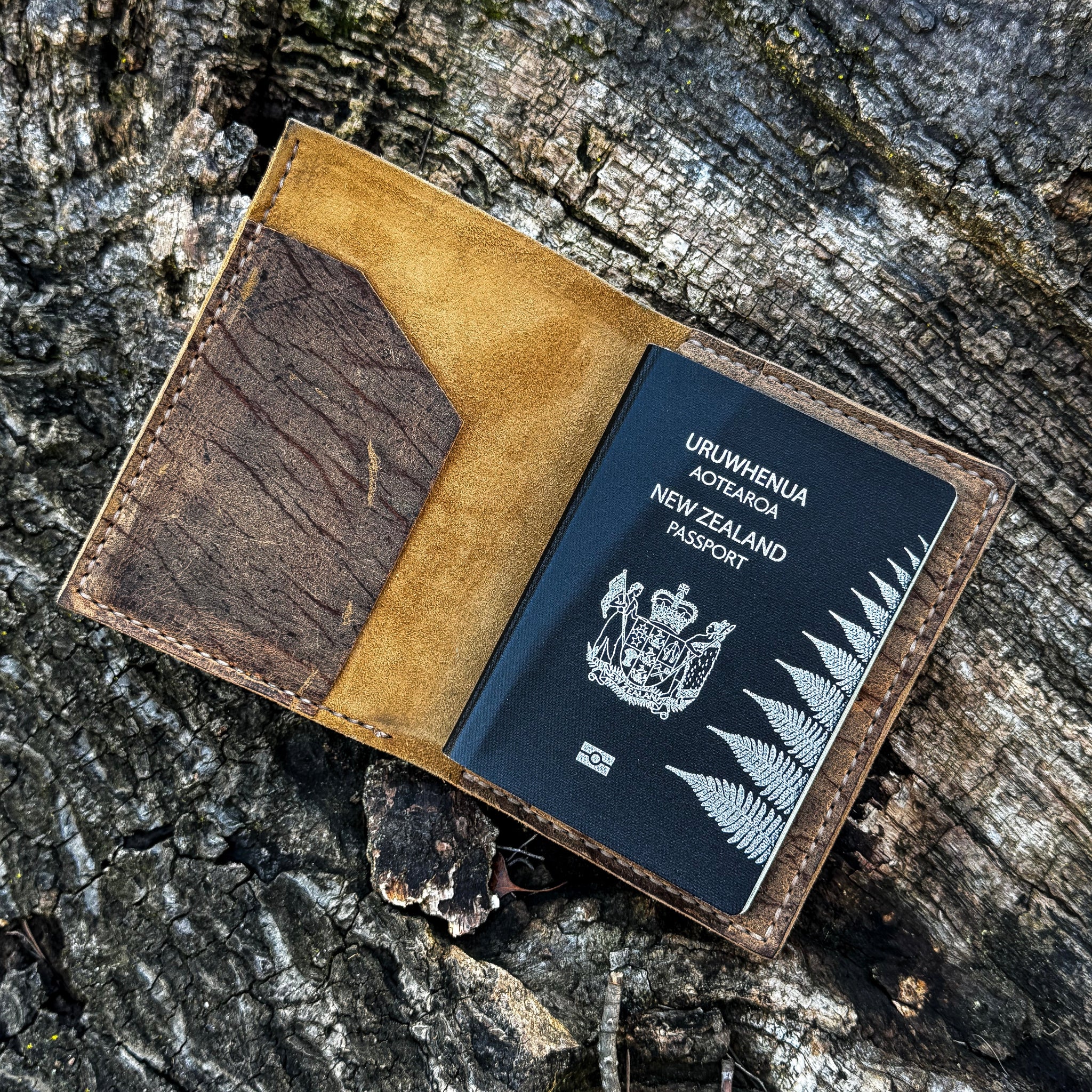 The interior view of the open No. 4 Journeyman Passport Wallet crafted from Baobab Wild African Kudu leather. The image displays a black New Zealand passport tucked securely into the right-hand pocket, highlighting the contrast between the soft golden suede inner lining, the heavily textured dark brown leather, and the precise hand-stitching, resting on a rugged tree bark background.