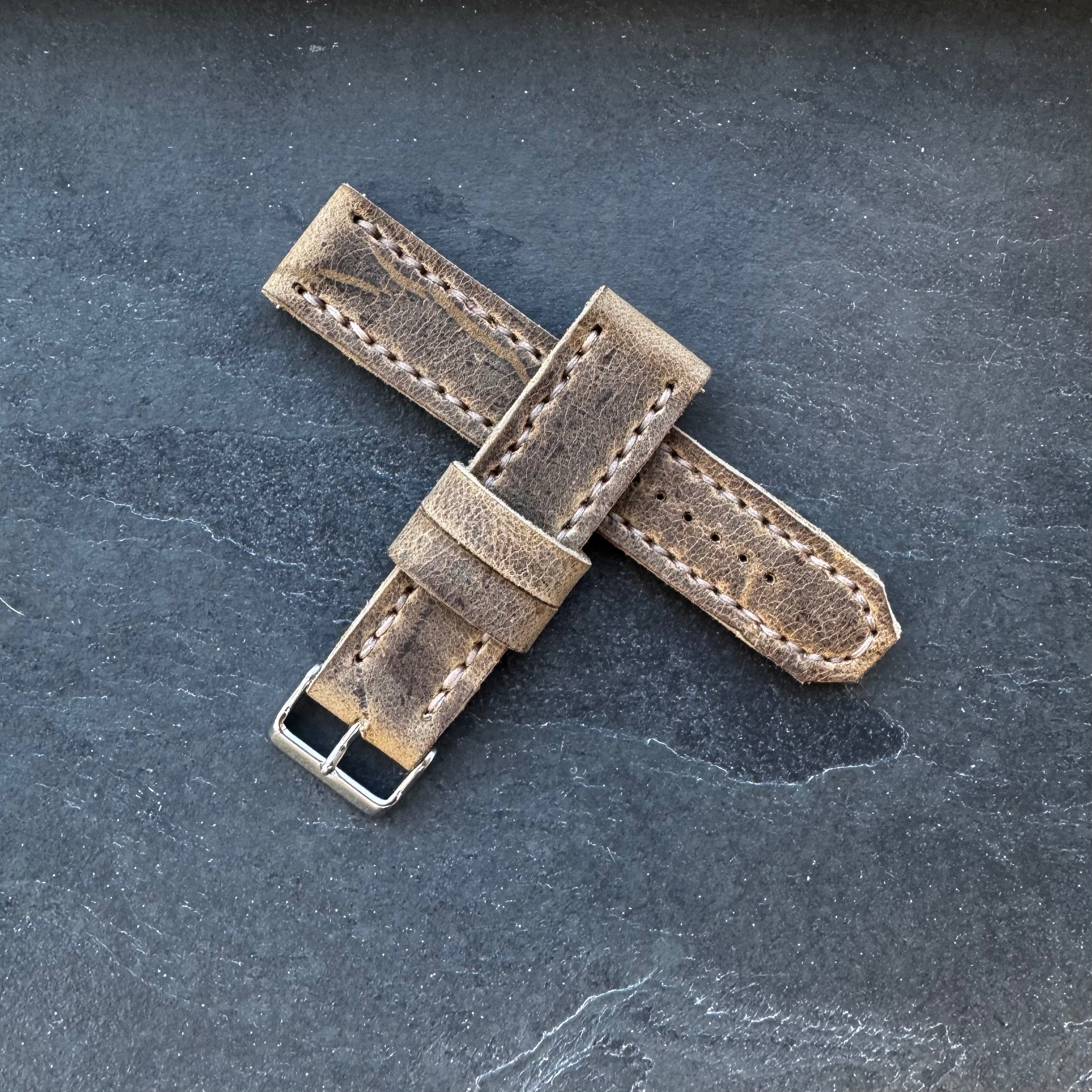 The No. 44 AVIATOR Leather Watch Strap in Wild African Kudu arranged in a crossed formation on a dark, textured surface.