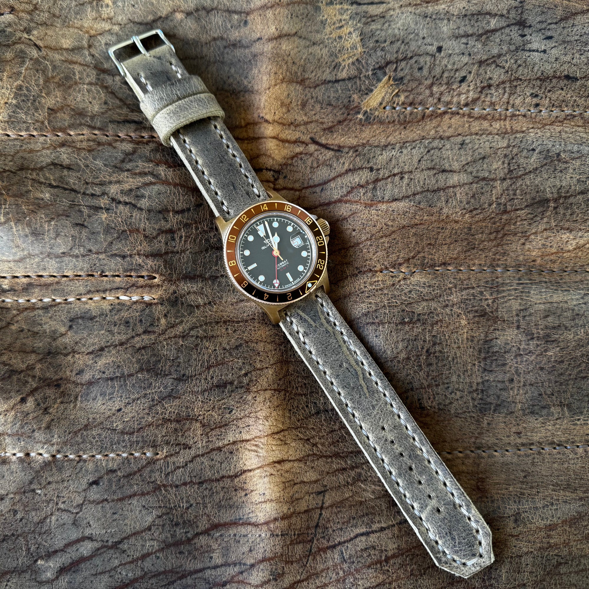 A close-up of a watch equipped with the No. 44 AVIATOR Leather Watch Strap in Wild African Kudu, resting on a rustic, distressed leather surface.