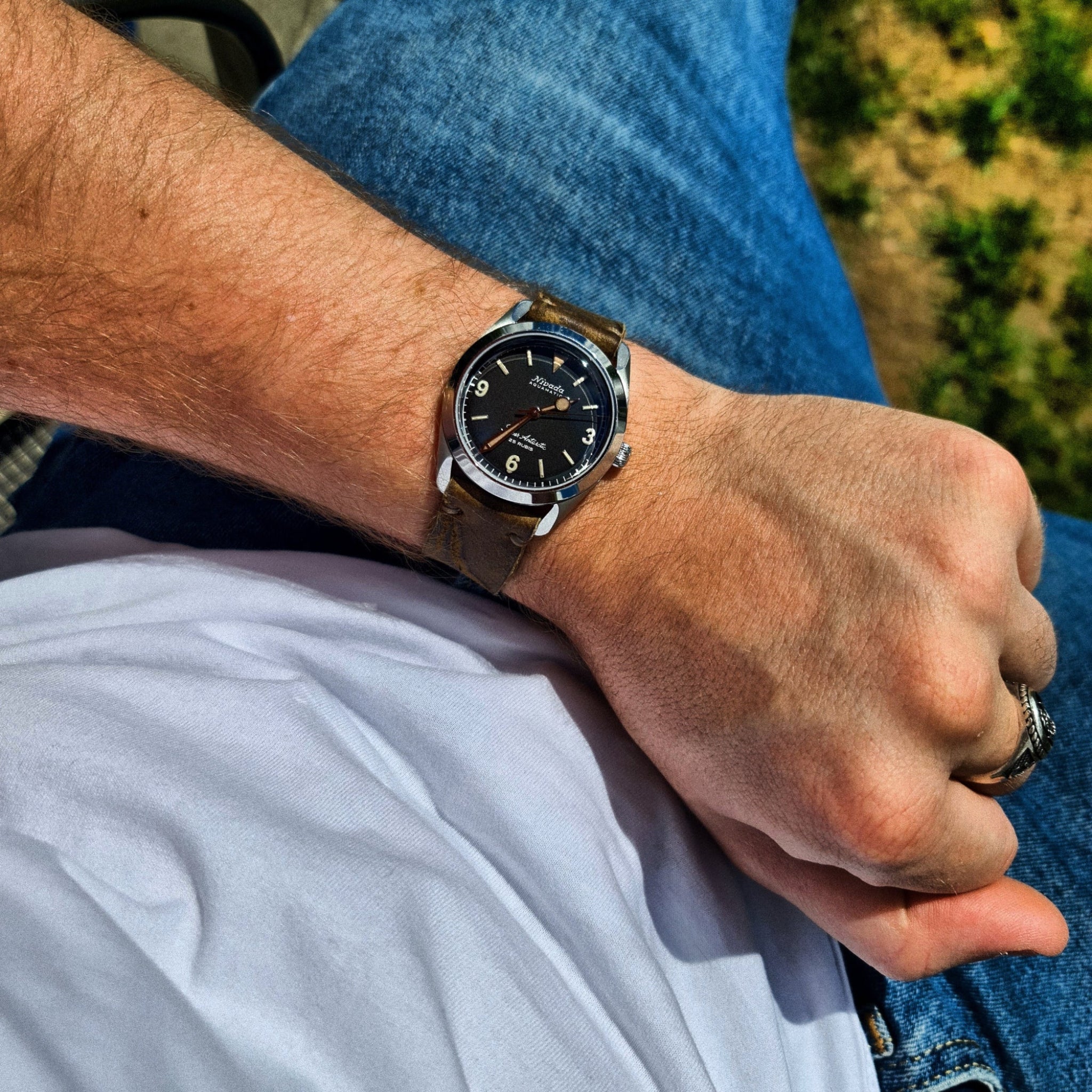  A lifestyle shot showing the No. 53 EXPLORER Leather Watch Strap in Vintage Wild African Kudu being worn on a wrist. The distressed, rugged light brown leather strap is paired with a black-dial vintage-style watch, styled casually with blue jeans and a white t-shirt outdoors.