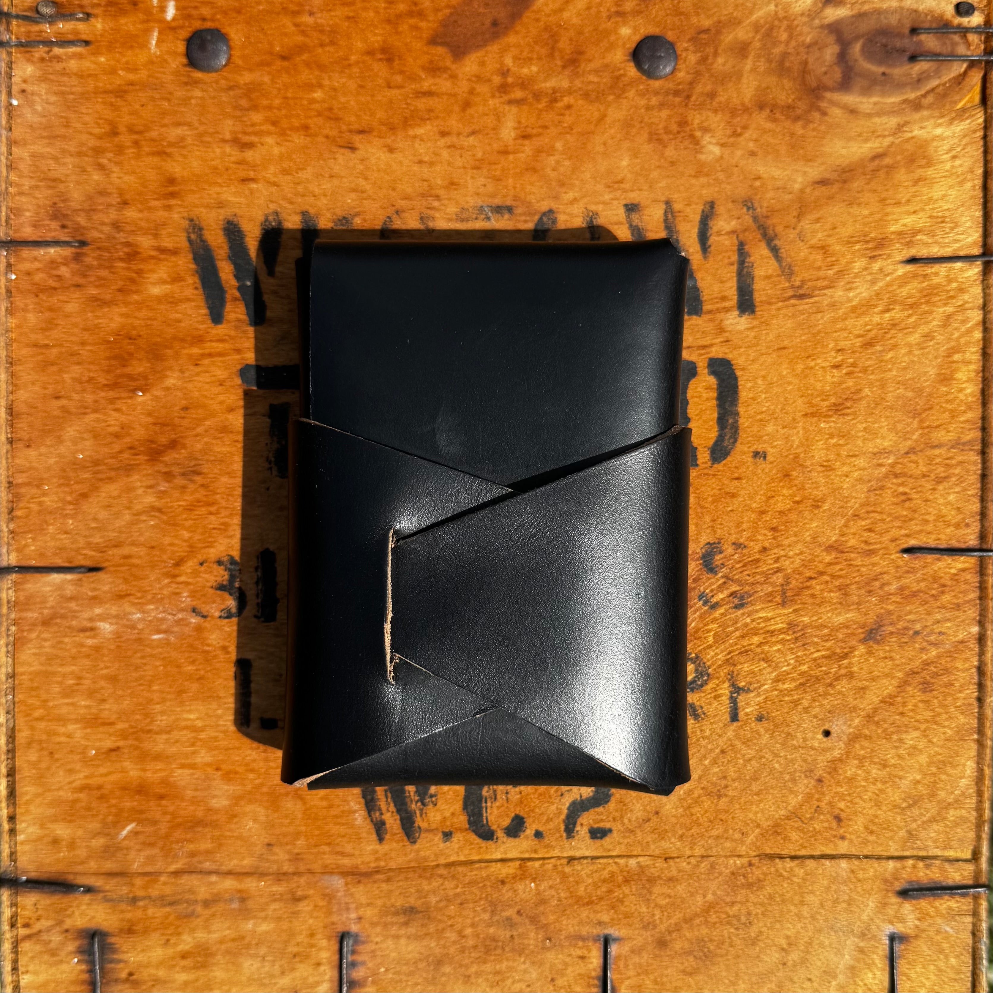 Closed angle view of the black No. 66 Woodsman leather fold wallet resting on a vintage wooden crate.