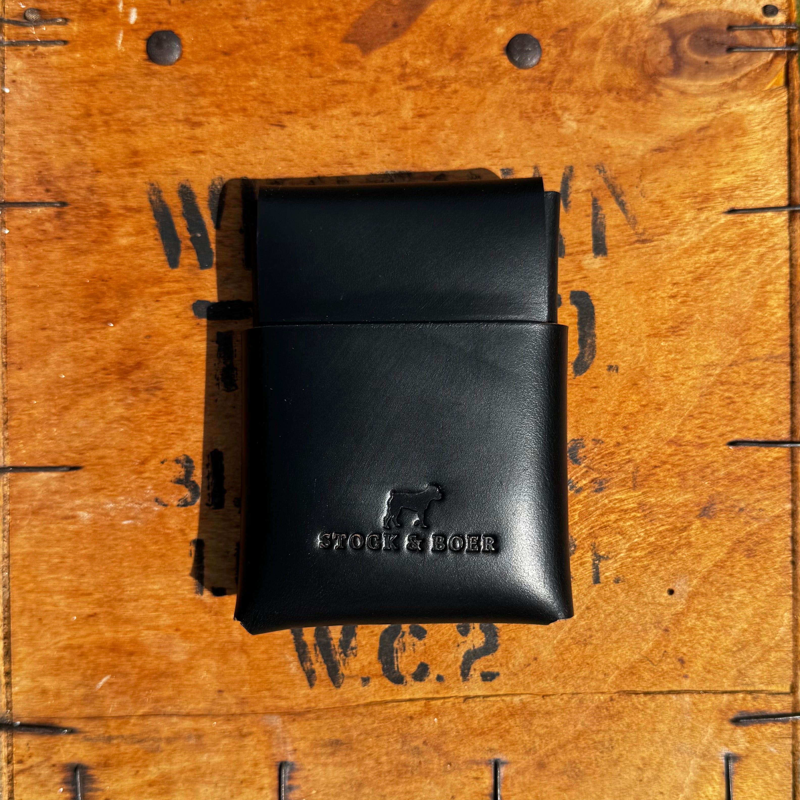 Closed front view of the black No. 66 Woodsman leather fold wallet, displayed on an antique wooden crate.
