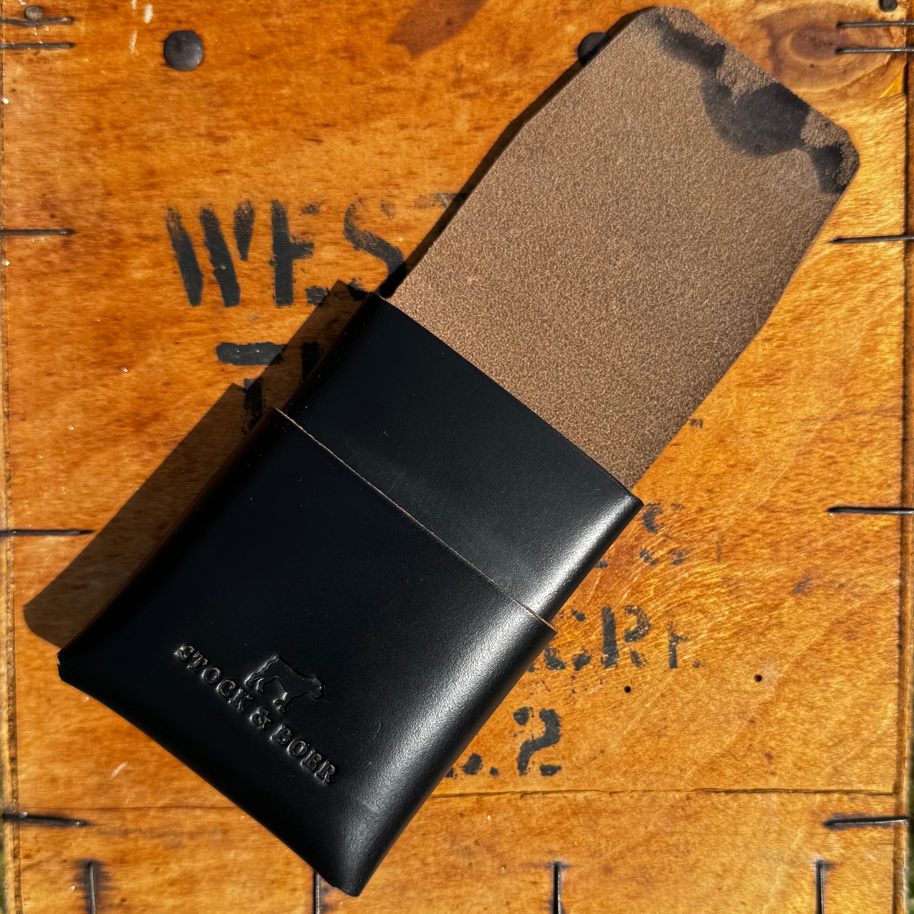 Partially open view of the black No. 66 Woodsman leather fold wallet, revealing the interior on a wooden crate.
