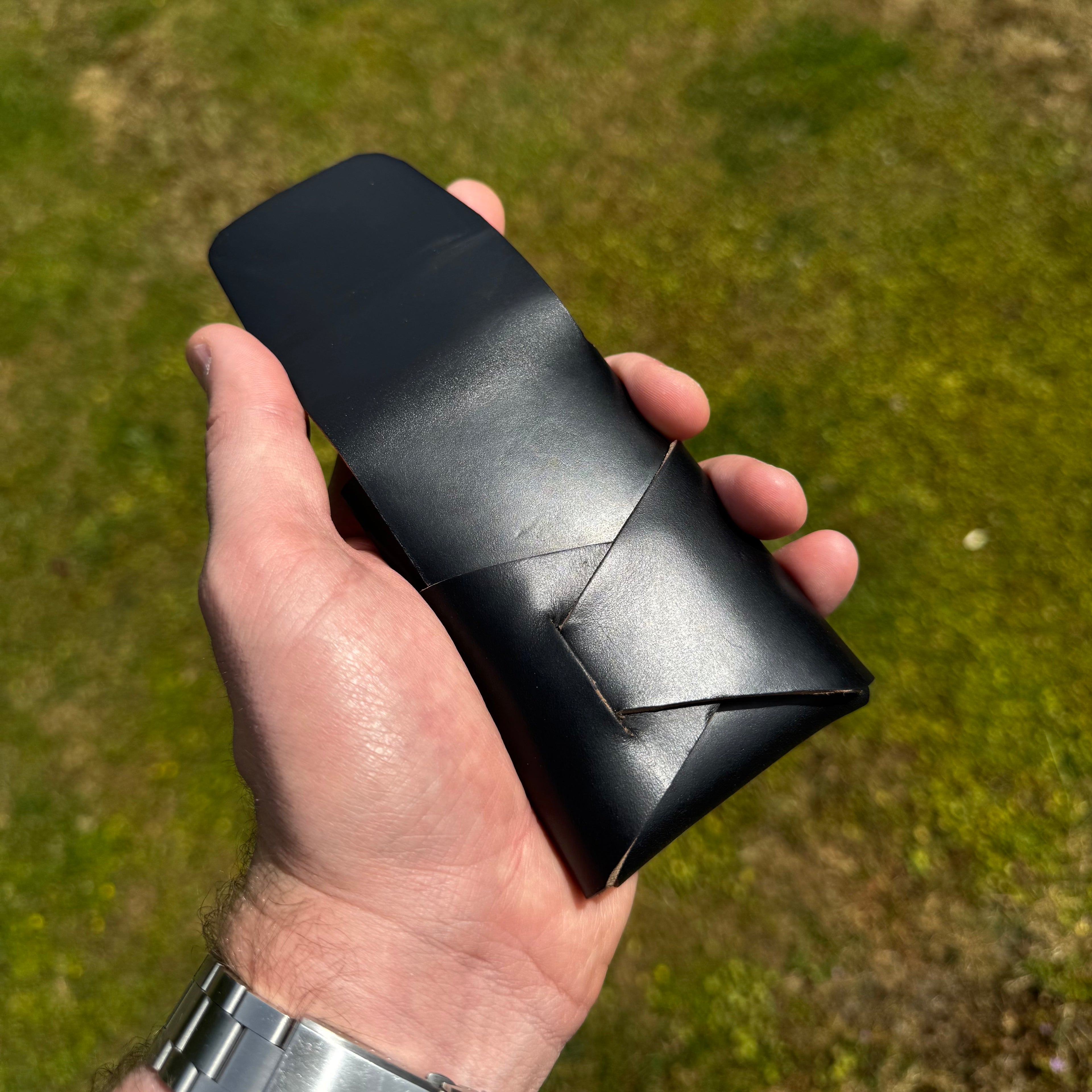 Handheld angled view of the black No. 66 Woodsman leather fold wallet in natural outdoor lighting.