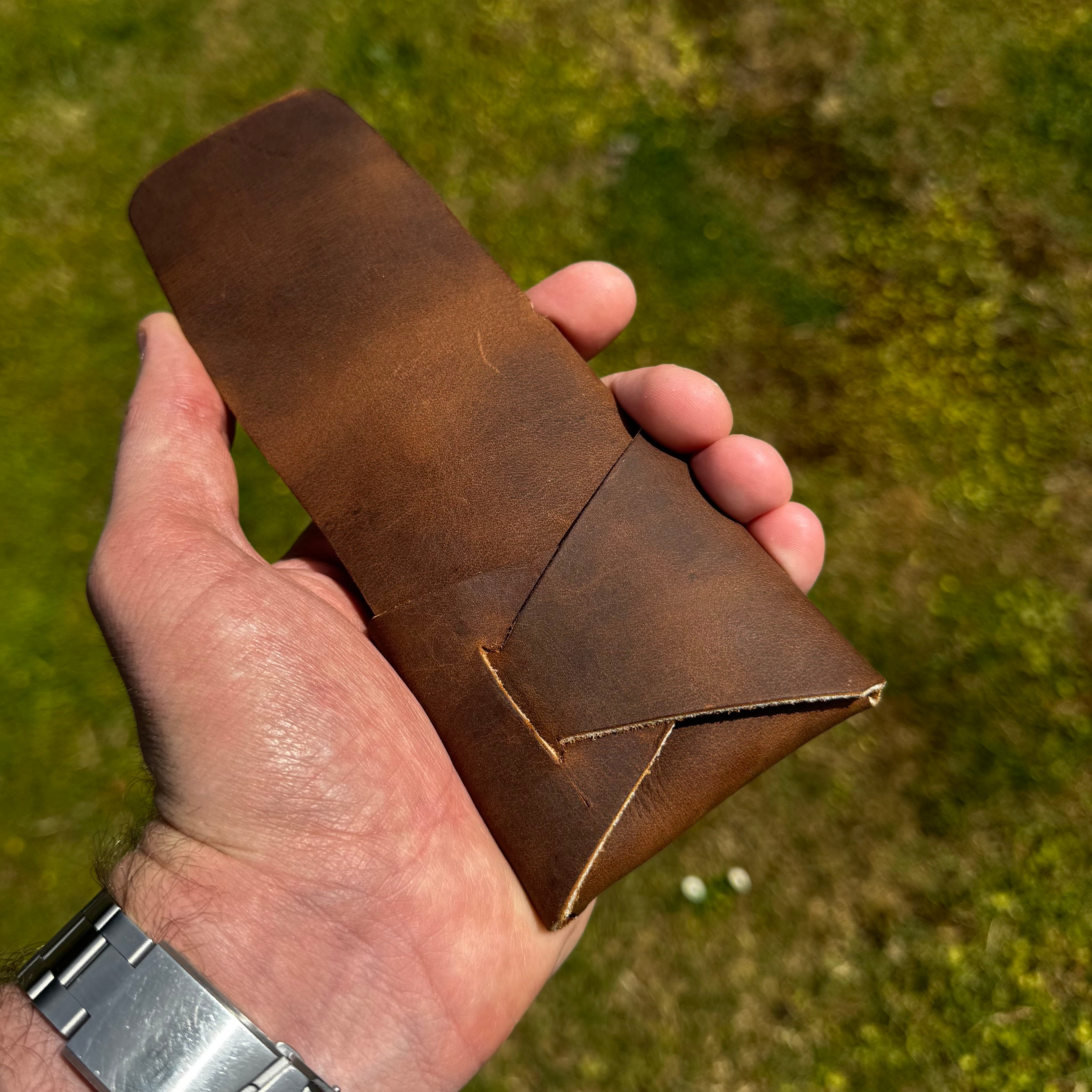 Handheld view of the closed No. 66 Woodsman leather fold wallet in Crazy Horse, held against a natural outdoor background.