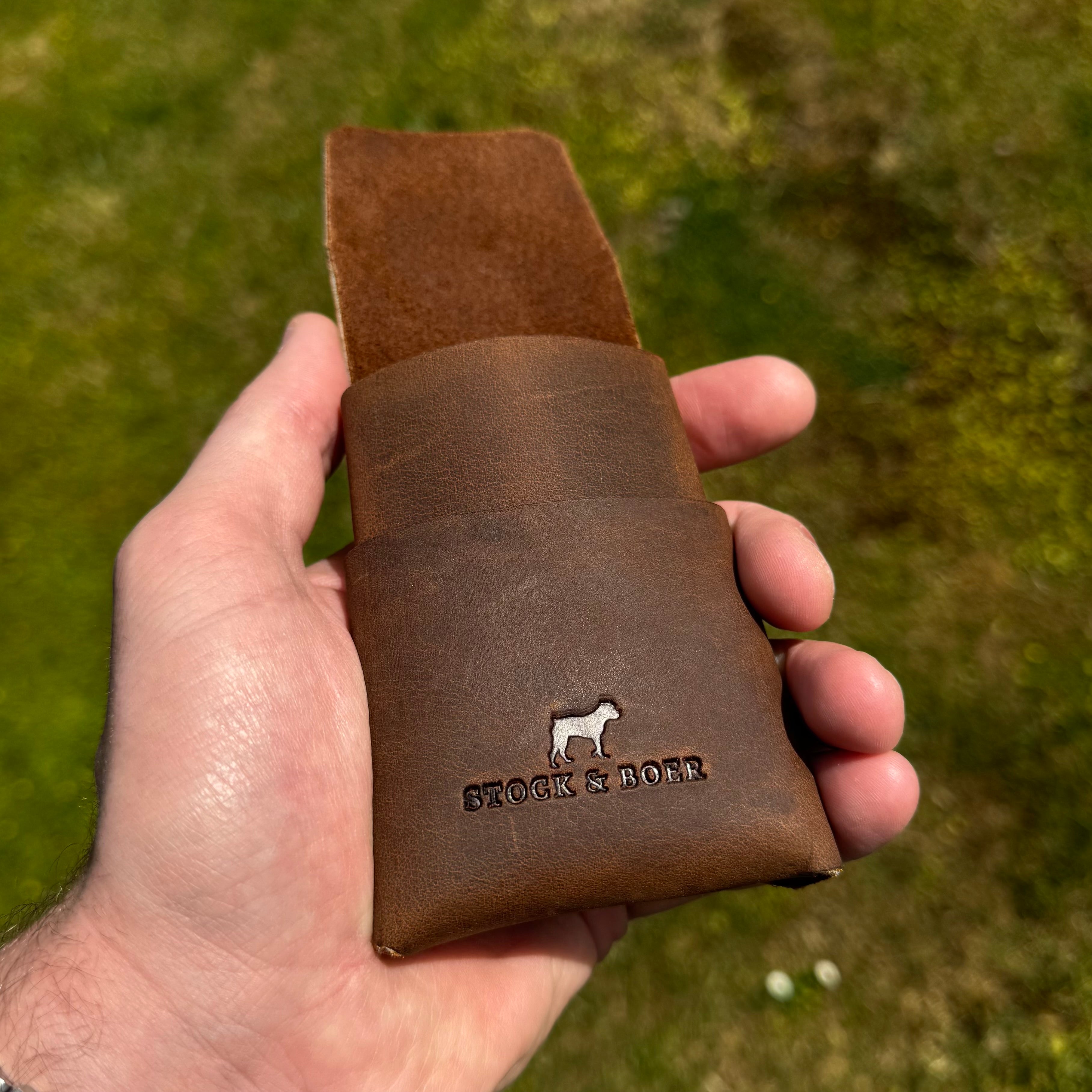 Close-up detail of the Stock & Boer logo embossed on the No. 66 Woodsman leather fold wallet in Crazy Horse leather, held outdoors.
