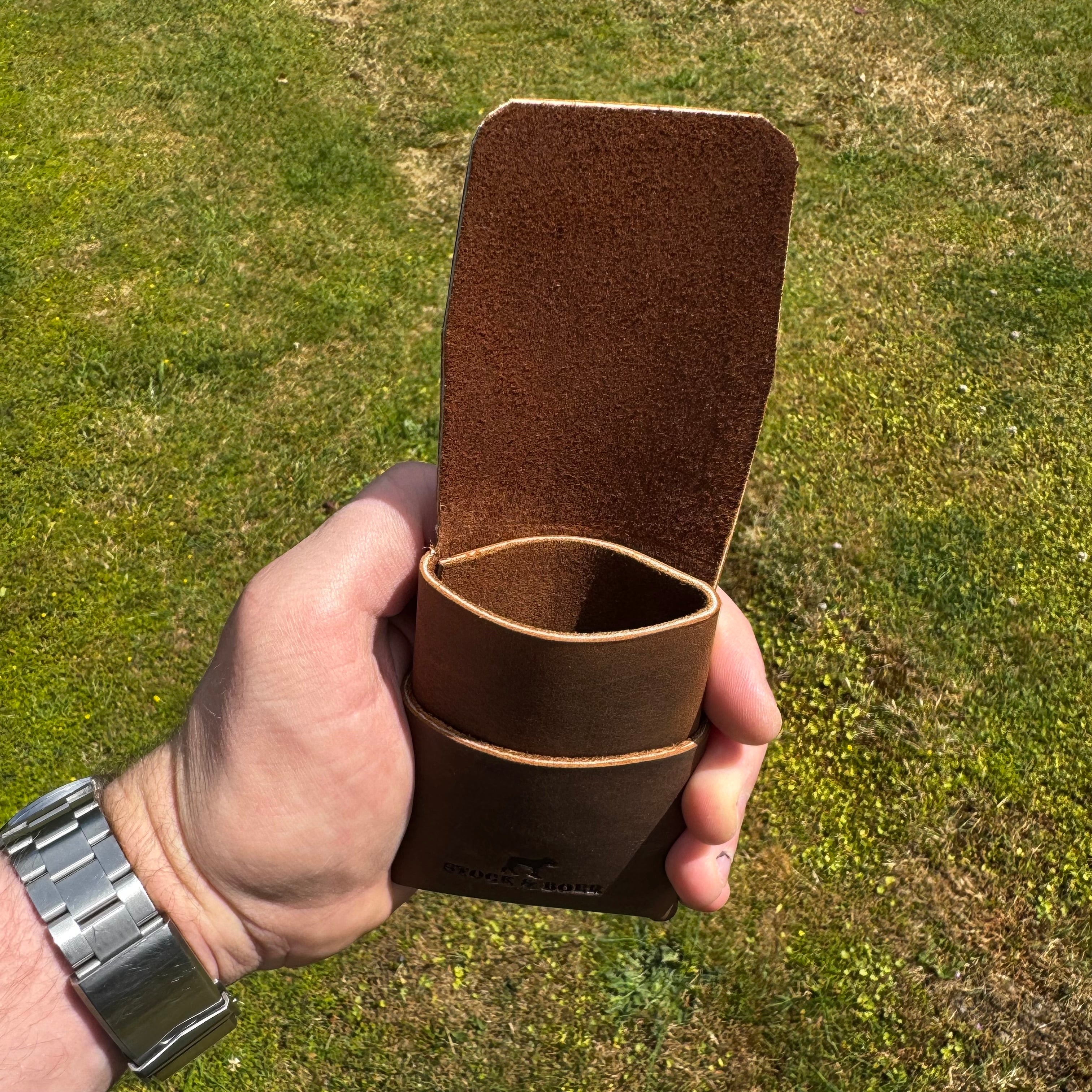 Side angle view of the No. 66 Woodsman leather fold wallet being opened, featuring durable Crazy Horse leather in natural outdoor lighting.