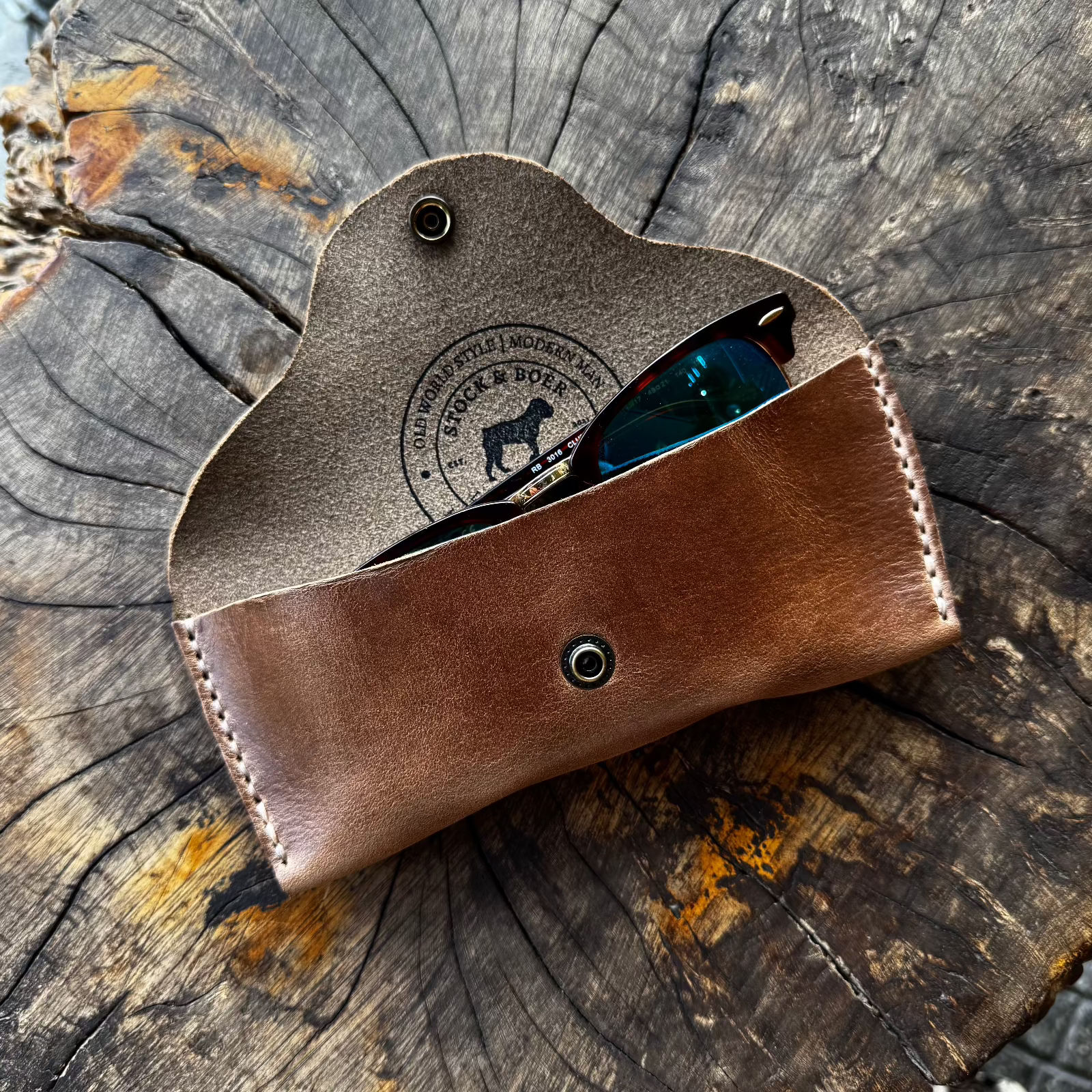 he open brown No. 7 DESPERADO Sunglass Case containing sunglasses, positioned on a tree stump.