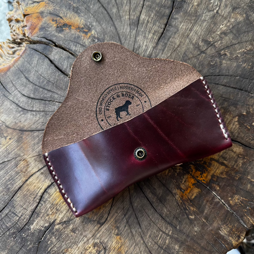 The open No. 7 DESPERADO Sunglass Case in burgundy Horween Chromexcel leather, resting on a weathered tree stump, featuring a visible Stock & Boer logo stamped on the interior.