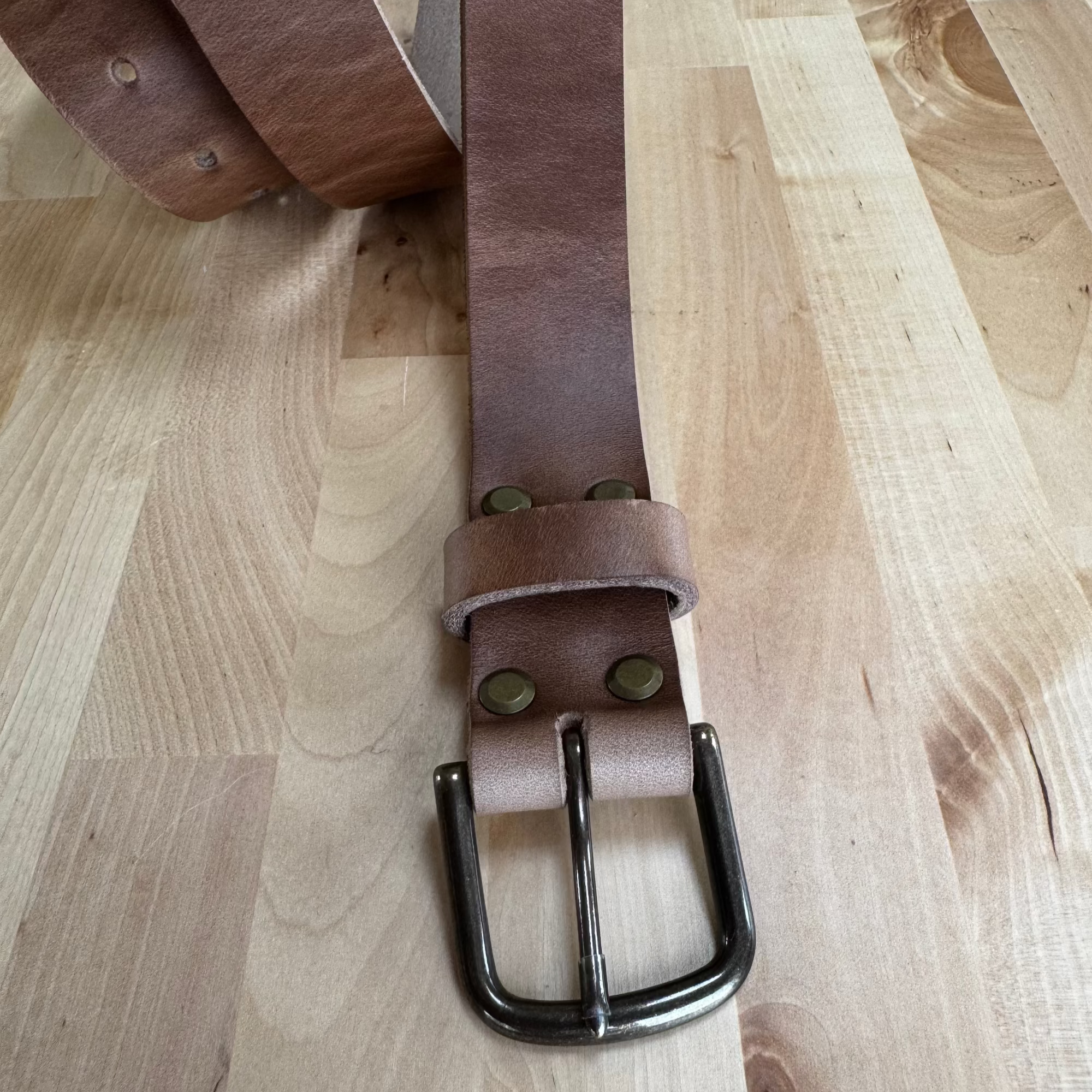 A flat-lay view of the No. 8 VAQUERO Full Grain Leather Belt crafted from natural Horween Chromexcel leather. The belt is laid out on a light-colored wooden surface, showcasing the buckle, rivets, and the smooth, natural finish of the leather.