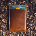 Leather No. 9 Ledger EDC pouch featuring the Stock & Boer logo, shown with a Yellowstone National Park notebook on a natural outdoor surface.