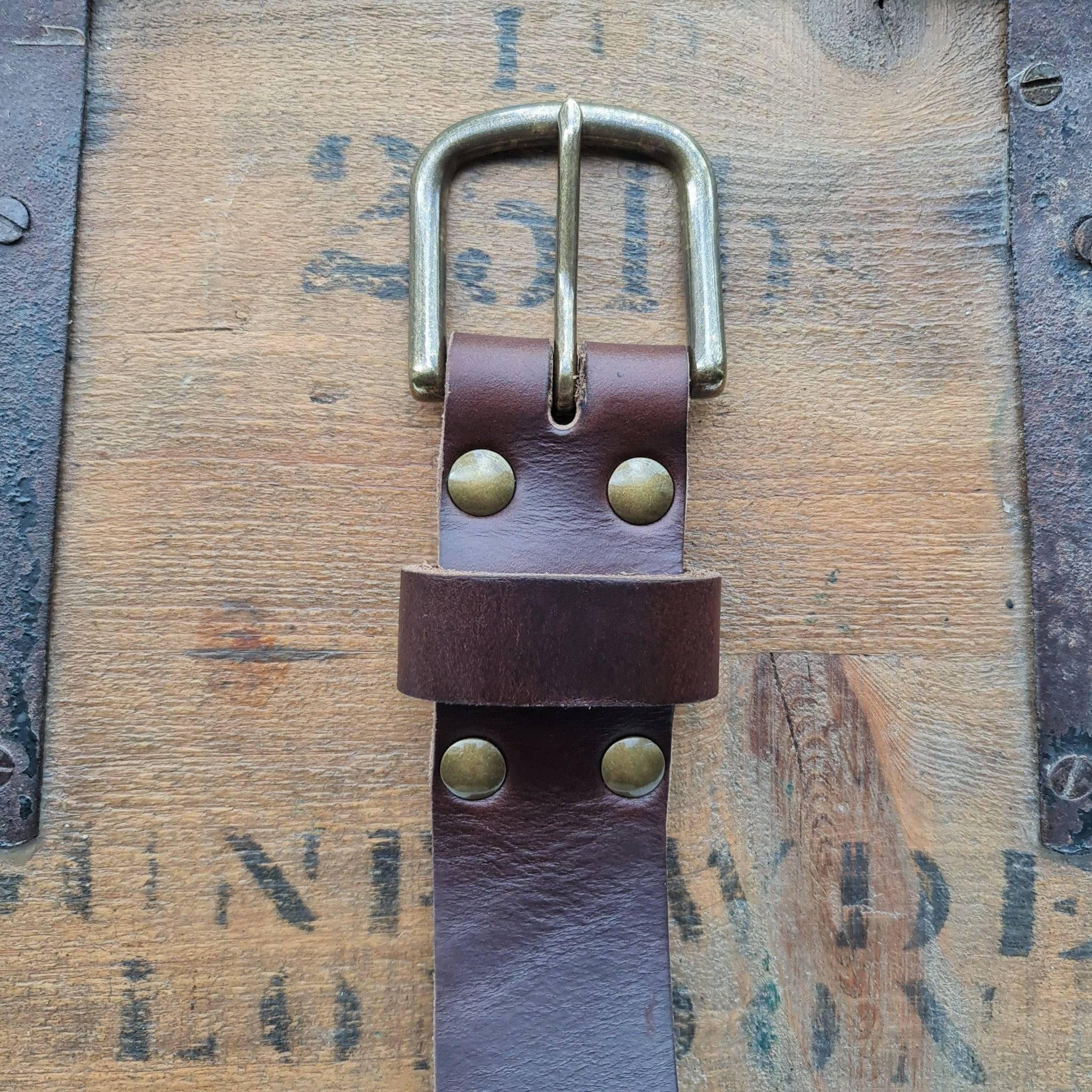 A close-up of a brown Horween Chromexcel leather belt buckle on a vintage wood background.