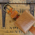 Close-up detail of a belt buckle and wallet bundle made from Horween English Tan Dublin leather, resting on a vintage wooden surface.