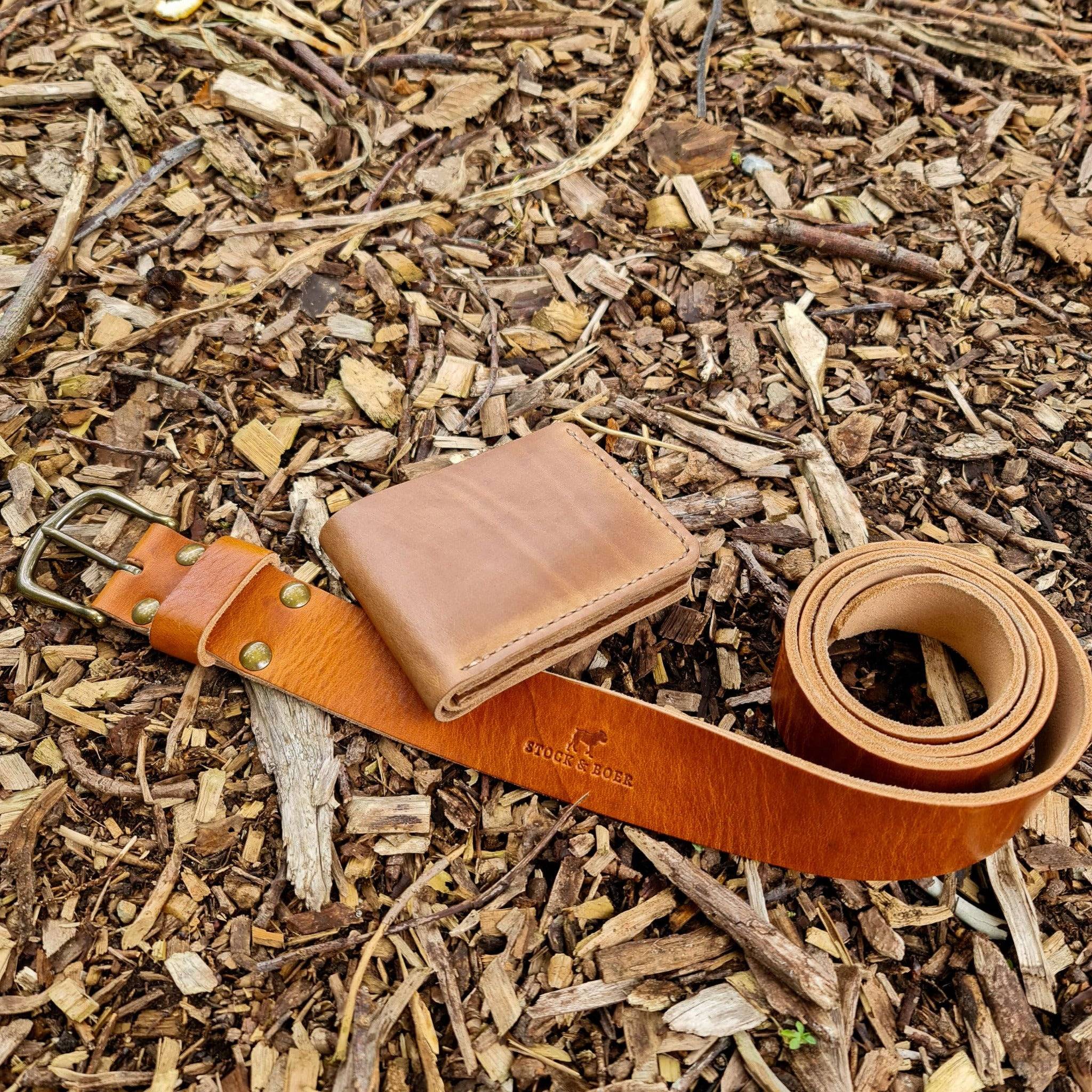 Flat lay view of the Horween English Tan Dublin leather wallet and belt bundle arranged on a wood chip ground.