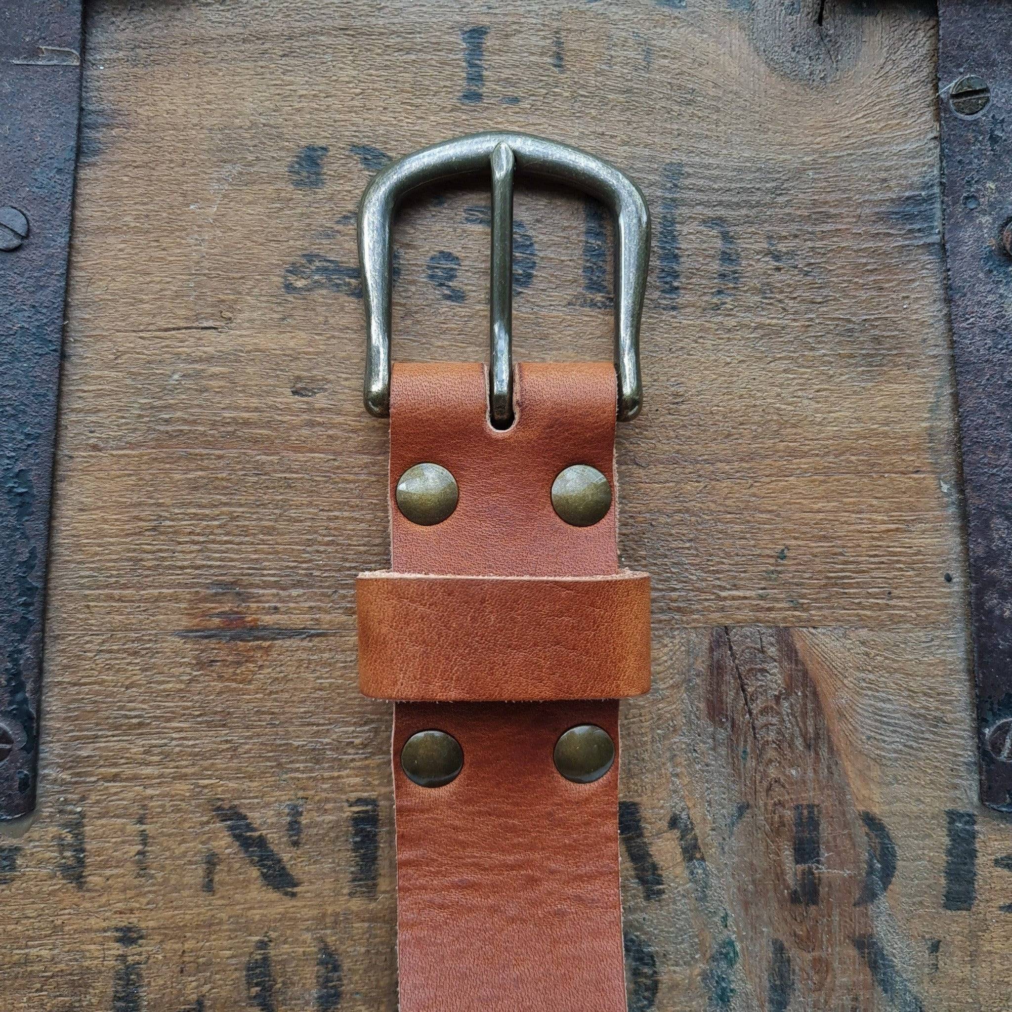  A close-up of a natural Horween English Tan Dublin leather belt buckle on a vintage wood background.