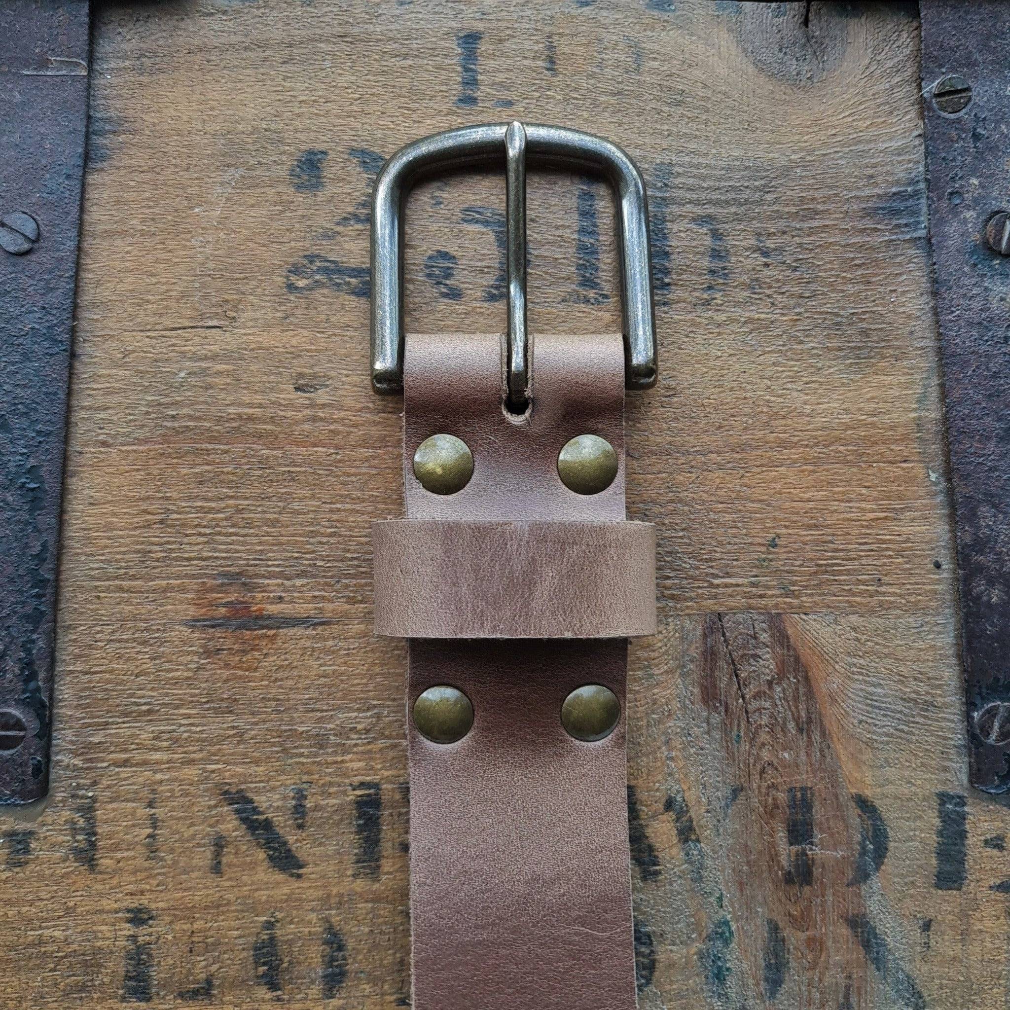 A close-up of a Horween Natural Chromexcel Leather belt buckle on a vintage wood background.