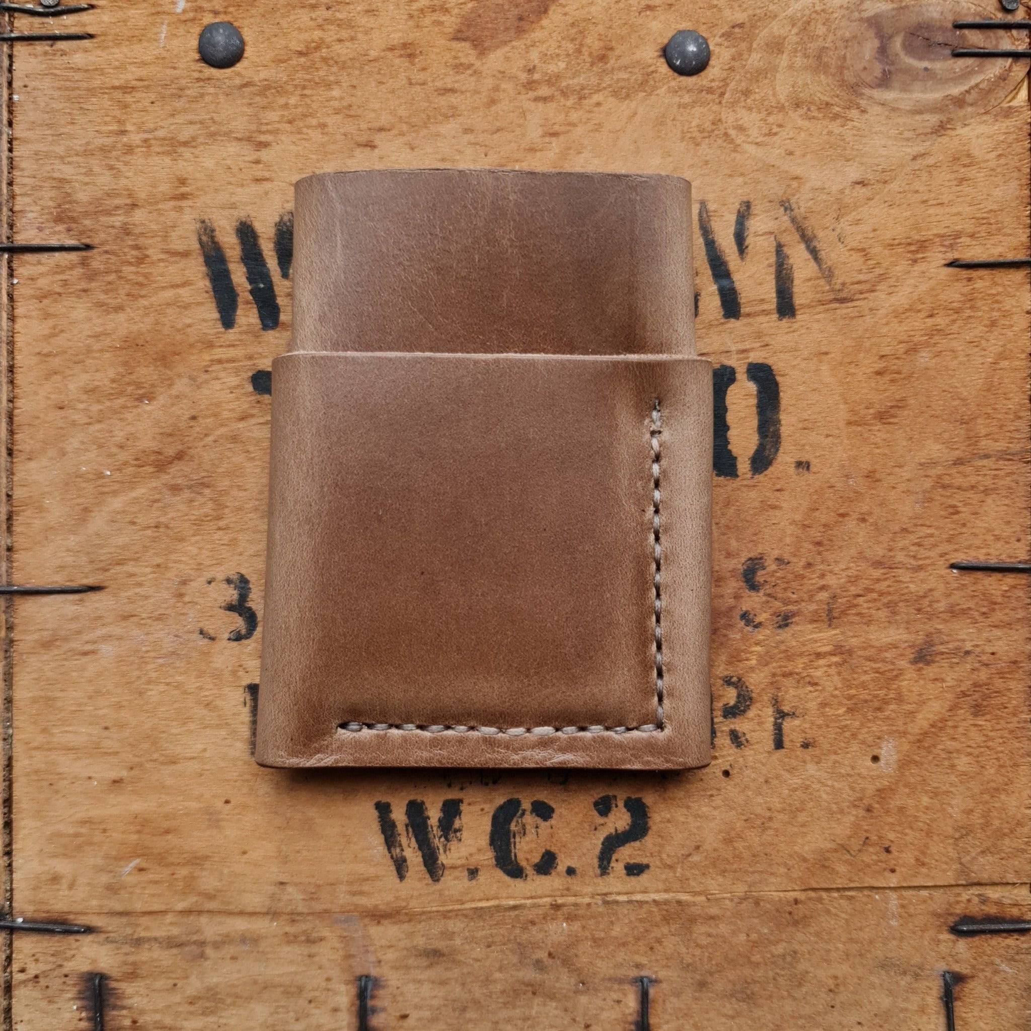 A flat-lay view of the No. 1835 TREKKER Front Pocket Wallet, crafted from natural Horween Chromexcel leather, resting on a vintage wooden crate. The image highlights the wallet's clean, minimalist design and detailed hand-stitching.