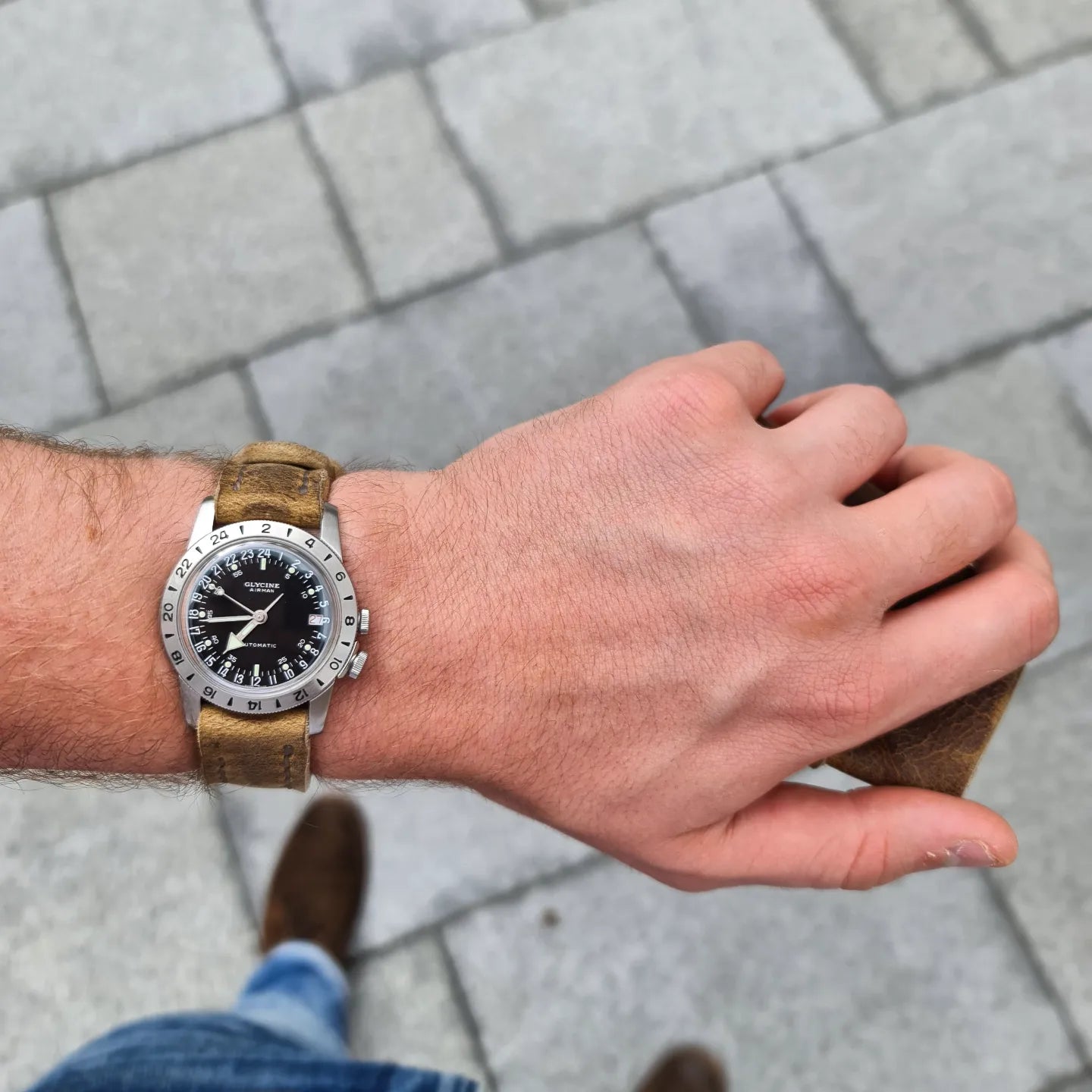 A lifestyle shot of a person wearing a watch with the No. 44 AVIATOR Leather Watch Strap in Wild African Kudu on their wrist, standing on a paved outdoor surface.