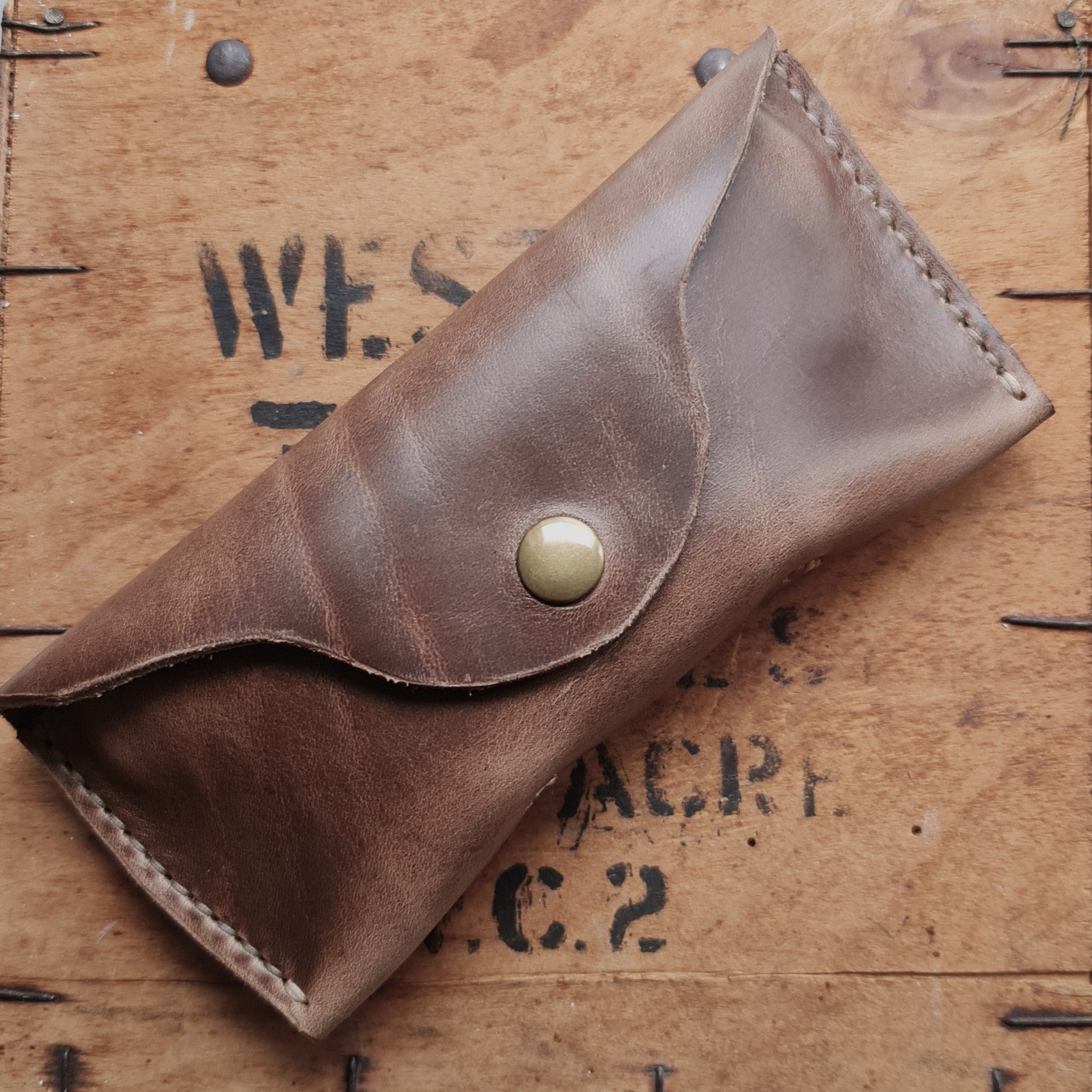 A closed tan No. 7 DESPERADO Sunglass Case resting on a rustic wooden crate with "W.C.2" markings.