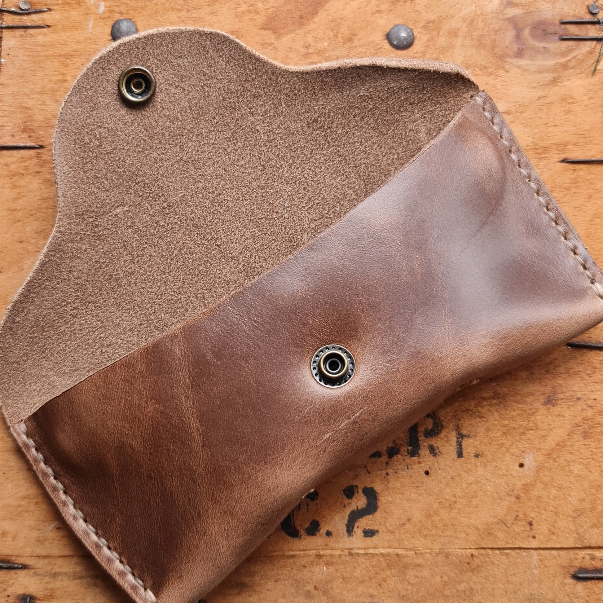 The open tan No. 7 DESPERADO Sunglass Case sitting on a wooden crate, displaying the interior suede and snap closure.